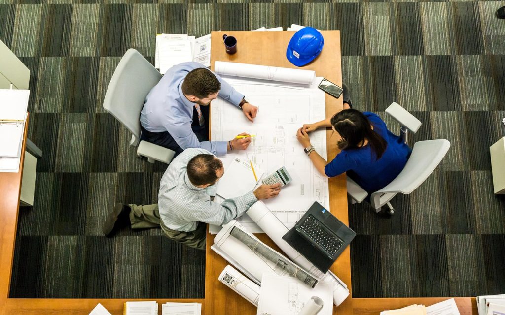 A group of people gathered around a desk in an office, reviewing blueprints and project plans together.
