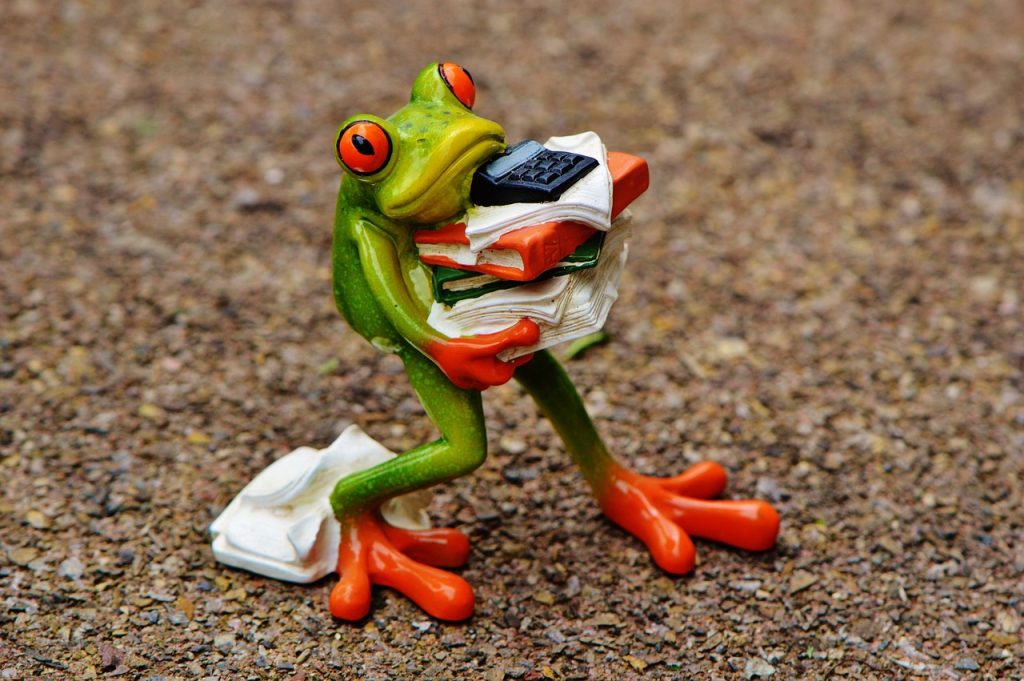 A ceramic green frog figure perched atop a stacked pile of office files, with a calculator nearby.